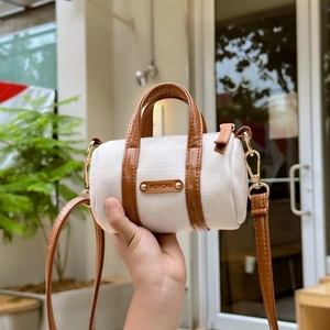Detail of canvas shoulder bag with brown leather trim and metallic brand plaque