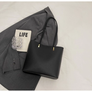 Detail of black pebbled faux leather tote bag with gold hardware on a grey blazer