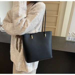 Detail of black pebble leather tote bag featuring gold hardware and slim shoulder straps