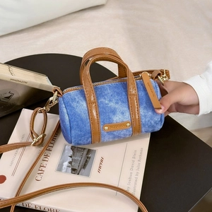 Detail of denim crossbody bag with brown leather trim and metallic brand logo plate