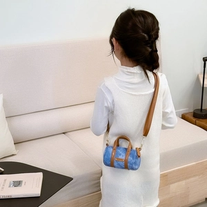 Blue denim mini cylinder bag with brown leather trim shown on model in a cozy interior