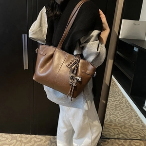 Detail of brown pleated PU leather tote bag with cat charm and buckle on female model