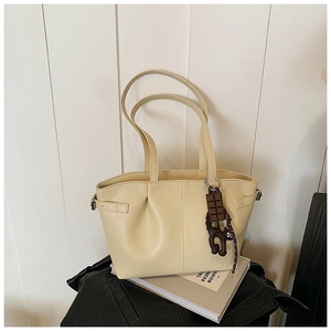 Detail of pleated cream PU tote bag with chocolate pendant on white striped background