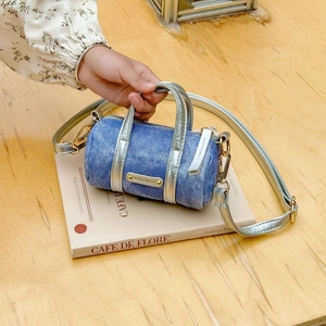 Detail of denim cylinder bag with silver metallic handle and KOYOKA logo on art book