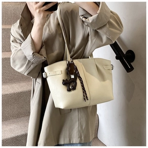 Detail view of creamy white tote bag with lychee grain leather and cat charm on stairs