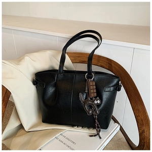 Detail of black pebbled PU leather tote bag with cute cat charm on a wooden chair