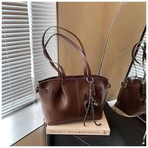 Detail of a brown PU leather tote bag featuring a cute black cat charm and side buckle