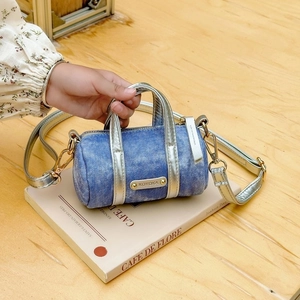 Chic blue denim mini barrel bag with silver metallic trim on a decorative book
