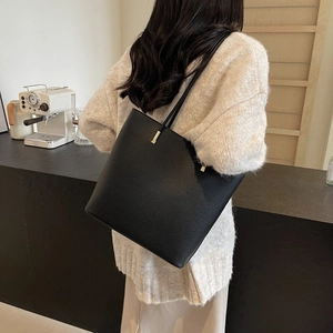 Classic black leather tote bag with gold hardware worn over the shoulder in a cafe setting
