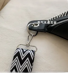 Detail of silver metallic clip and chevron woven strap on a black studded leather bag