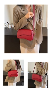 Detail view of red leather crossbody bag with curved base and magnetic flap closure