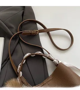 Detail of brown lychee grain leather handbag featuring silk scarf and pompom charm