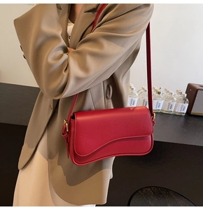 Detailed view of a red leather crossbody bag featuring a unique wave-shaped flap and gold buckle