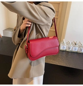 Detail of red lychee grain leather handbag with elegant wave-shaped flap and gold hardware