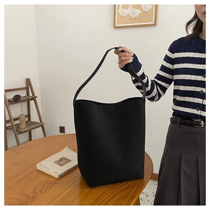Detailed view of the black canvas shoulder bag held by a model in a minimalist setting