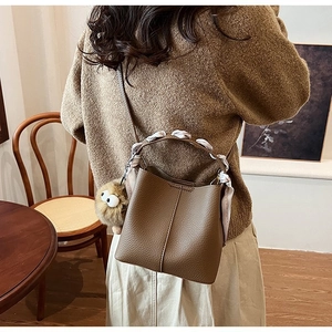 Close-up of brown litchi grain leather bucket bag with silk scarf and plush charm