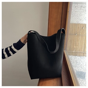 Close-up of minimalist black canvas tote bag with wide strap on a wooden windowsill