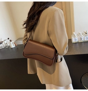 Detail of dark brown lychee leather shoulder bag with wave-cut flap and metal buckle