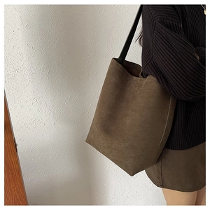 Close-up of brown suede hobo bag with black leather strap on model's shoulder