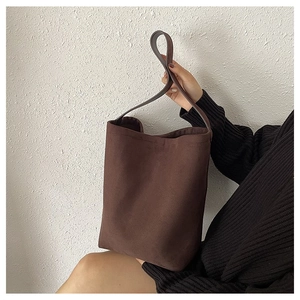 Detail of deep brown suede bucket bag with wide shoulder strap held by a model