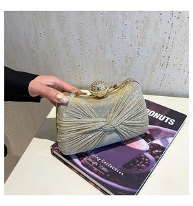 Détail de pochette de soirée dorée avec texture satinée plissée et fermoir boule diamant