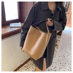 Close-up of a large brown suede bucket bag worn by a model in a cozy indoor setting