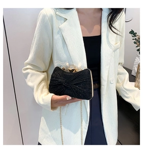 Détail de la pochette de soirée noire avec design plissé, boucle cristal et chaîne dorée