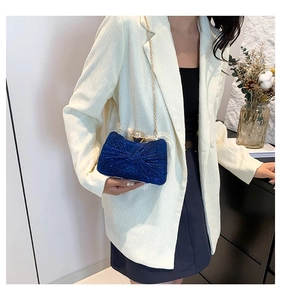 Détail de la pochette de soirée à paillettes bleu marine avec nœud et chaîne dorée sur blazer