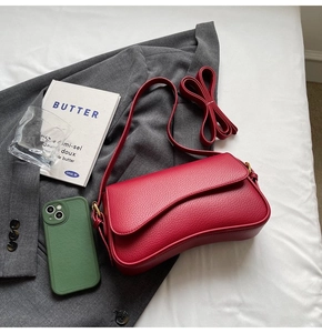 Detailed view of red lychee grain leather handbag with asymmetric curved flap design