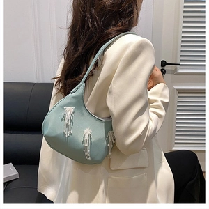 Dettaglio della borsa hobo blu acqua con frange di nappe bianche indossata dal modello