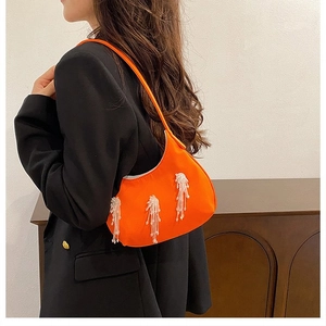 Dettaglio borsa a mezza luna arancione con nappe di perline bianche su blazer