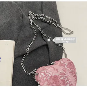 Detail of pink heart-shaped nylon bag with white embroidery and silver chain strap