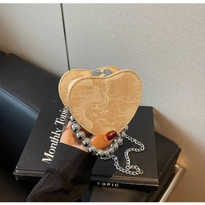 Detail of a beige heart-shaped denim handbag with silver bead handle and chain strap