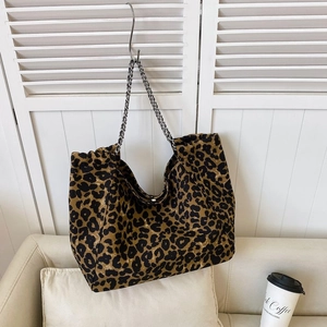 Macro detail of large leopard print tote bag with metallic chain straps in a home setting