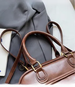 Close-up of a dark brown faux leather handbag with golden hardware and long shoulder strap
