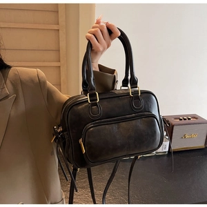 Detail of black faux leather handbag featuring golden hardware and front zipper pocket