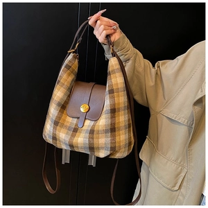Detail of vintage plaid handbag with leather flap and golden round buckle on khaki trench coat