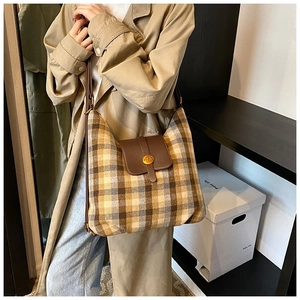 Brown plaid crossbody bag with leather flap and gold buckle worn as a shoulder bag