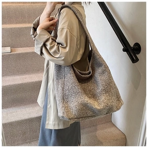 Grand sac cabas gris texturé porté à l'épaule par un mannequin dans un décor minimaliste