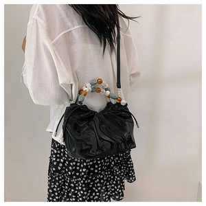 Details einer schwarzen Plissee-Tasche mit bunten Perlengriffen an einem Frauenmodel