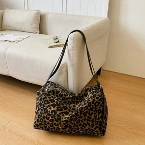 Large leopard print canvas tote bag with black leather straps on a sofa