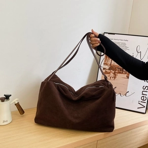 Close-up of large dark brown suede tote bag with zipper and slim straps in a home setting