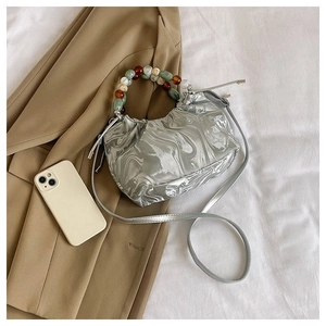 Detail der silbernen Tasche in Liquid-Metal-Optik mit buntem Perlengriff und Schultergurt