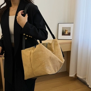 Detail of camel suede tote bag featuring black leather strap and gold metal rivets