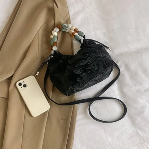 Detail der schwarzen Plissee-Tasche mit buntem Marmorperlen-Griff auf weißem Bettzeug