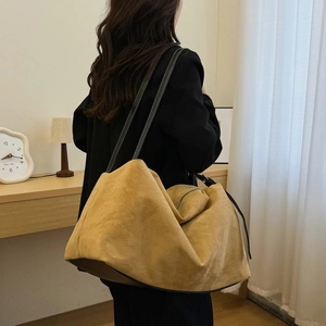 Detail of a khaki suede tote bag with contrast stitching on leather straps for autumn