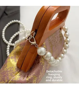 Détail du sac rose à texture dorée, poignée en bois et chaîne en perles amovible