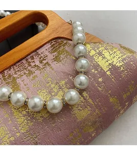 Gros plan du sac rose avec finition dorée, bandoulière en perles et poignée en bois
