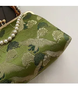 Detailed embroidery of white cranes and pine on green satin with bamboo handle