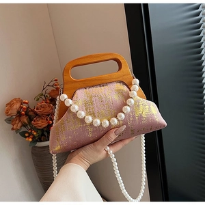 Détail du sac bandoulière rose avec texture dorée, poignée en bois et chaîne de perles